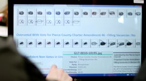 An image of a person using a touchscreen monitor to review overvotes.